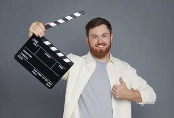 Poster - Making movie. Smiling man with clapperboard showing thumb up on grey background