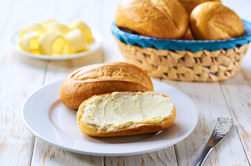 Wall Mural - Basket of bread with butter on white wooden table.