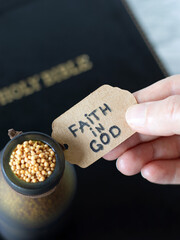 Wall Mural - Hand-holding handwritten note: Faith in God on a bottle with mustard seeds and holy bible book in the background. Top view. Trust and belief in Jesus Christ, Christian biblical concept.