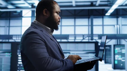 Poster - African american man walking in high tech facility, using laptop to patch network issues leading to slow data transfer rates. Data center worker fixing errors affecting supercomputers, camera A