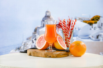 Poster - Glass of fruit juice on wooden board table top with blurred building background on sunny hot day in summer.