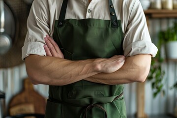 Wall Mural - A man in a kitchen apron. Chef work in the cuisine. Cook in uniform, protection apparel. Job in food service. Professional culinary. Green fabric apron, casual stylish clothing. Handsome baker posing,