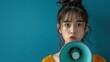 © pengedarseni - Japanese woman with yellow casual clothes, big huge blank screen area, scream in megaphone isolated on plain blue color background Lifestyle concept.
