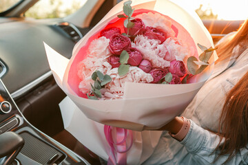 Girl with a large bouquet of peonies in a car at sunset