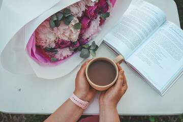 Canvas Print - A bouquet of peonies, an open book and a cup of tea in hands, a pleasant time in nature