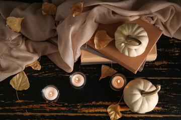 Wall Mural - Burning candles, scarf, pumpkins, books and autumn leaves on black wooden background