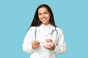 Poster - Portrait of female dentist with dental mirror and jaw model on blue background