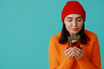 Sticker - Beautiful young woman with glass of hot mulled wine on blue background