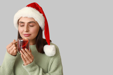 Poster - Beautiful young woman in Santa hat with glass cup of hot mulled wine on grey background