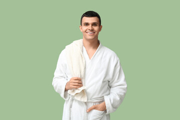 Wall Mural - Portrait of handsome young man in bathrobe with towel on green background