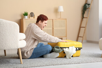 Wall Mural - Emotional young man packing suitcase at home