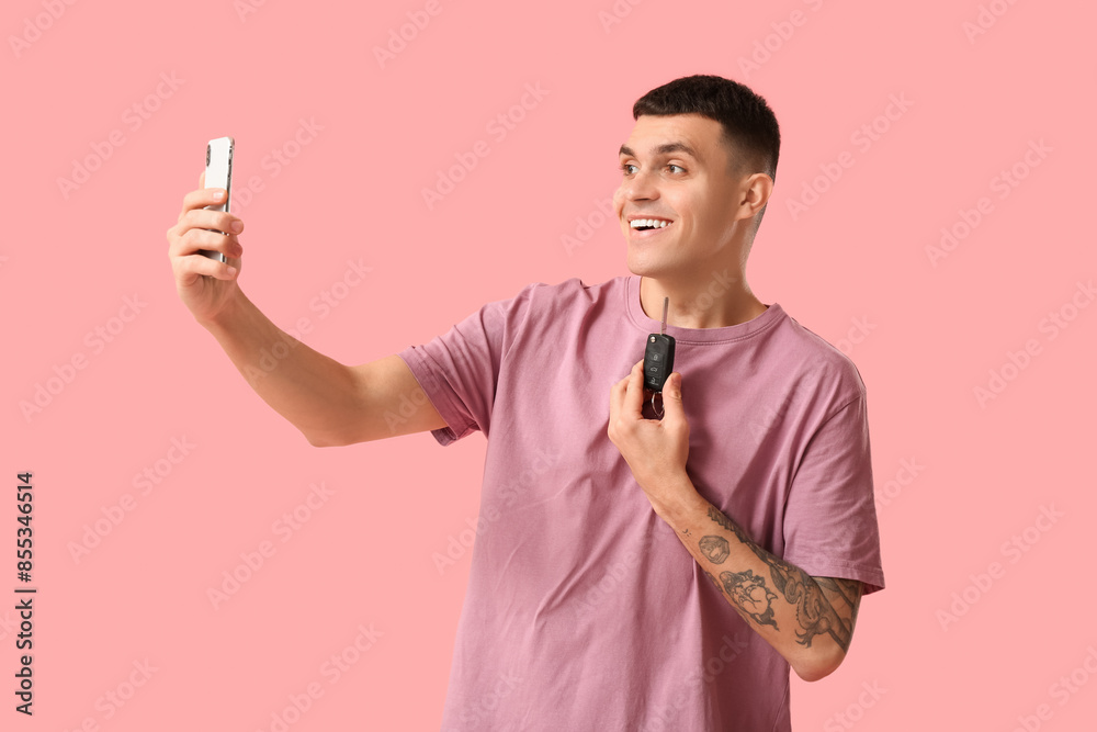 Young man with car key taking selfie on pink background