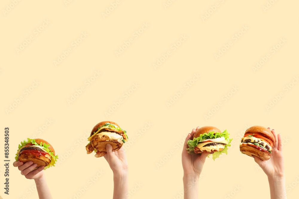 Female hands with tasty burgers on light yellow background
