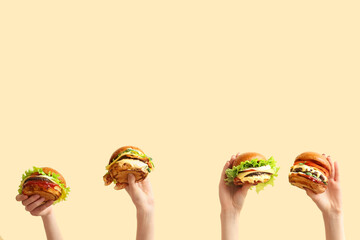 Wall Mural - Female hands with tasty burgers on light yellow background