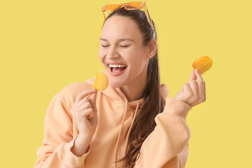 Canvas Print - Young woman eating potato chips on yellow background, closeup