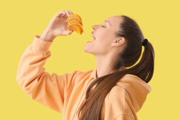 Canvas Print - Young woman eating potato chips on yellow background, closeup