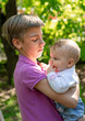 © sommersby - Teenage boy with short blonde hair holds his baby sister, who is wearing white shirt and denim pants. Boy is looking down at baby, who is smiling and chewing on her fingers