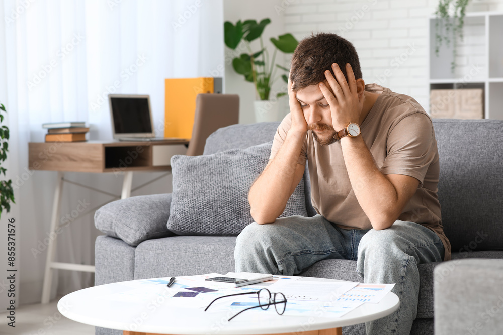 Stressed young man in debt sitting on sofa at home