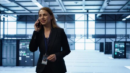Poster - Software engineer talking on smartphone in data center, coordinating server maintenance tasks. Woman surrounded by server racks and high tech equipment, speaking during telephone call, camera A