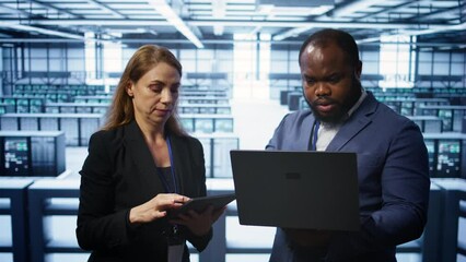  - system administrators in data center overseeing server operations using notebook and tablet. colleag