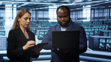  - system administrators in data center overseeing server operations using notebook and tablet. colleag