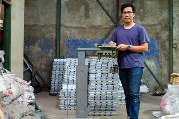 a southeast asian man weighing bar zinc (aluminium) using old style scale in the warehouse and writi