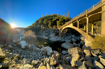 Panoramic view of the old and modern Route 49 arch bridge. Sun being the mountain and highway. Low river water level with rocky surface. South Yuba River State Park, Nevada County, California USA.