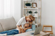 © SHOTPRIME STUDIO - Mother and child bonding on a cozy couch with a laptop, surrounded by bookshelves filled with books