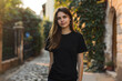 © alfi - Female model wearing black t-shirt on a bright street for urban mockup design template
