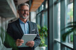 © Varitnan - Happy elderly businessman holding tablet in office.