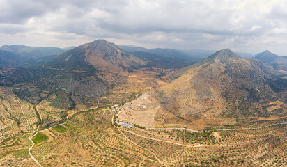 Wall Mural - Mycenae, Greece. Mycenae - Excavation site. Greek settlement of the 12th century BC. e. with the ruins of the acropolis, palace and tombs. Summer day. Cloudy weather. Summer. Aerial view
