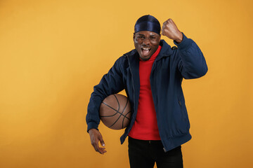 With basketball ball. Handsome black man is in the studio against yellow background