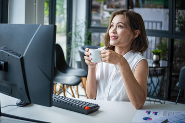 Wall Mural - Businesswoman sitting at desk on couch in workplace or at home working on laptop and analyzing data on charts and graphs and writing on papers to make business plan and strategies for company, startup