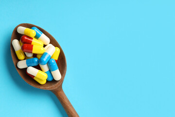 Wall Mural - Many antibiotic pills with wooden spoon and space for text on light blue background, top view. Medicinal treatment