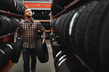 Male mechanic holding car tire in automobile store