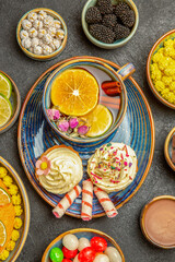 Wall Mural - top close-up view a cup of herbal tea a plate of cupcakes with cream a cup of herbal tea with lemon and sweets next to the bowls of berries citrus fruits white candies on the dark table