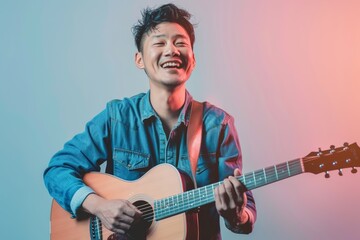 Wall Mural - Portrait of a cheerful asian man in his 20s playing the guitar on pastel or soft colors background