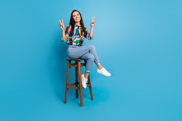 Sticker - Full length photo of nice cheerful woman wear print shirt sitting on bar stool two hands showing v-sign isolated on blue color background