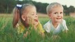 © maxximmm - little girl showing her tongue to her brother lying on the grass in the park. happy family kid dream concept. small children play in the summer in nature in the park in fun the green grass