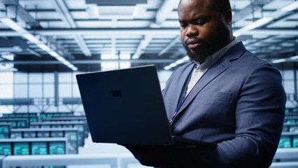 Poster - Computer scientist in high tech facility using laptop to patch network issues affecting server cabinets performance and connectivity, leading to poor client communication, camera B