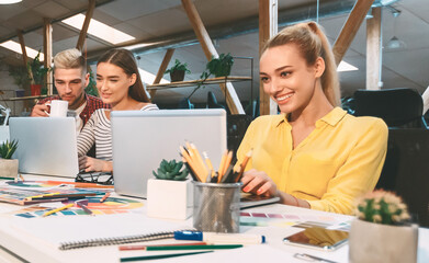 Poster - Several individuals sitting around a table, each with a laptop open and engaged in work or discussion.