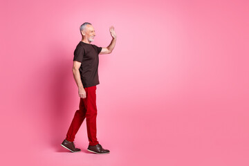 Sticker - Full size photo of cheerful senior man dressed brown t-shirt red trousers go empty space say hello isolated on pink color background