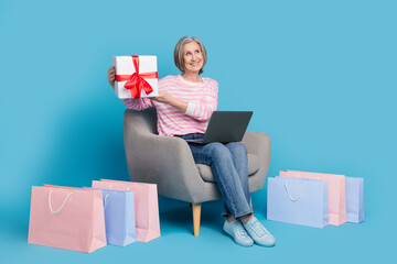 Poster - Full length photo of lovely pensioner lady armchair netbook shopper gift dressed stylish striped garment isolated on blue color background