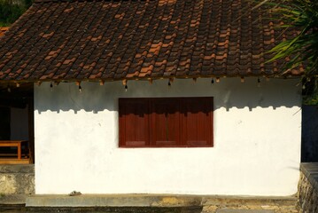 old house with white wall, wooden window and clay roof tile in a summer day