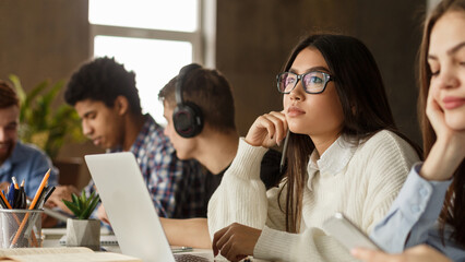 Wall Mural - Studying in college library. Thoughtful girl using laptop, preparing for final exam