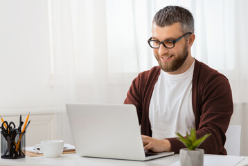 Aufkleber - A man is seated at a desk, focused on his laptop computer screen. His hands are typing on the keyboard while he looks intently at the display. The workspace is organized