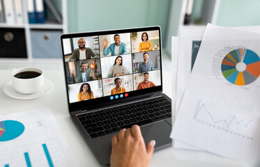 Poster - A close-up image of a laptop screen showing a business team participating in a video conference meeting. The laptop is positioned on a white table with data charts