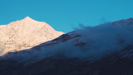 Wall Mural - Morning fog above the snow covered Himalayan mountain peaks during the winter season as seen from Keylong in Lahaul, Himachal Pradesh, India. Fog covers the snowy mountain during early morning.