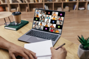 Poster - A person sits at a desk, taking notes on a notepad while participating in a video conference meeting on their laptop computer.