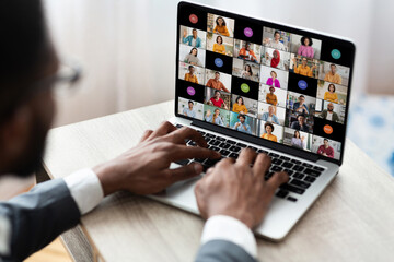 Poster - Black man in a grey suit and white shirt sits at a desk using a laptop to participate in a video conference. His hands are on the keyboard and the laptop screen shows participants in a video chat